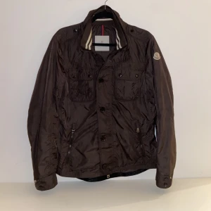Moncler ”mate” field jacka - Tjena, säljer nu min moncler ”mate” field jacka som i princip är som ny! Nypris: 7000 kr, Skick: 9/10, färg: mörk brun, size: 177-187 CM beroende på hur man vill att den ska sitta passar det flera längder. För mer info eller bilder skicka ett meddelande!