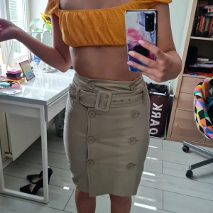 Beige kjol med knappar - Snygg kjol med knappar och skärp samt en slit i bak. Köpt på Humana förra året och bara använd ett fåtal gånger. I bra skick. Står storlek 38 men tycker mer den känns som 36. Funkar även till 34 med skärpet. 