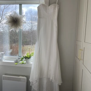 Oanvänd bröllopsklänning  - Oanvänd bröllopsklänning med spetsdetaljer och litet släp. Sitter mycket smickrande på kroppen.