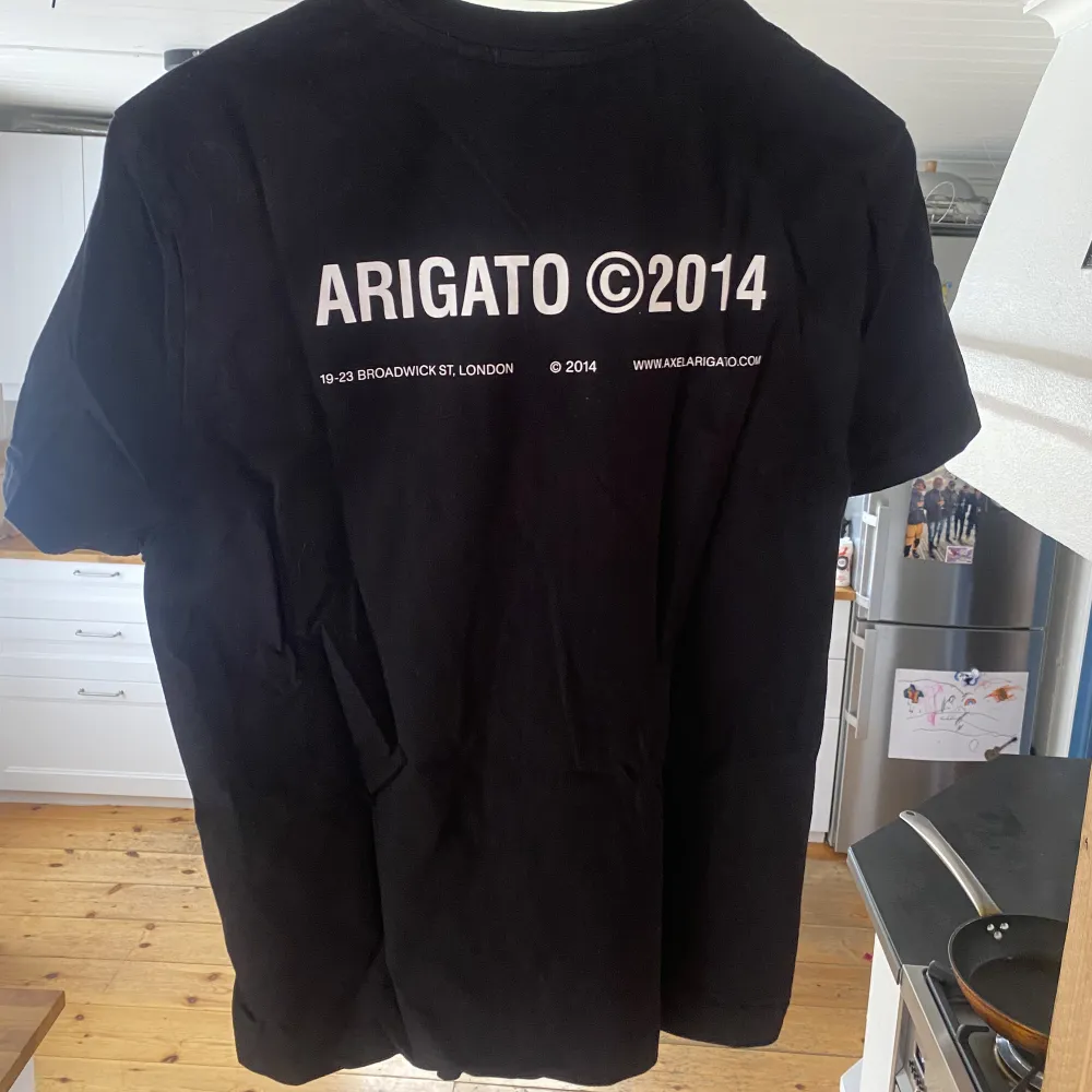 Svart Axel Arigato T-Shirt med vit text. Skrynklig då den inte använts men då den endast är använd ett fåtal gånger är den fortfarande i väldigt fint skick. Köpt för 800kr. T-shirts.