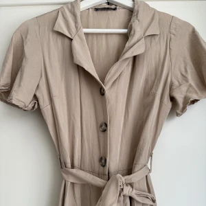Beige byxdress - Skön byxdress från NA-KD (Trendyol) i Strl 36 med knyte i midjan. Använd 1 gång