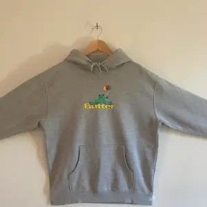 Denna hoodie är från Butter och har ett tryck på framsidan med en groda och loggan. Den har typ tre minimala röda färgprickar på fickan som man ser på tredje bilden. Förutom det är den i fantastiskt skick. Pris kan variera. 