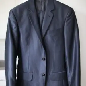 Mörkblå kostym i blankt/glansigt material. Märke Indochino. Passar för personer runt 175 cm & 70 kg. Byxorna är uppsydda och kan göras ~5 cm längre.  Finns i Luthagen, Uppsala.