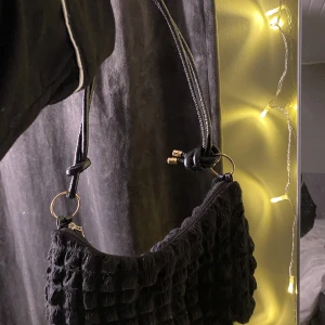 Väska - En svart lite mindre väska med guld detaljer och ett band som passar bra runt axeln. Använd ett fåtal gånger och i bra skick. Köpt för ca 100:-. Pris kan diskuteras. 💕