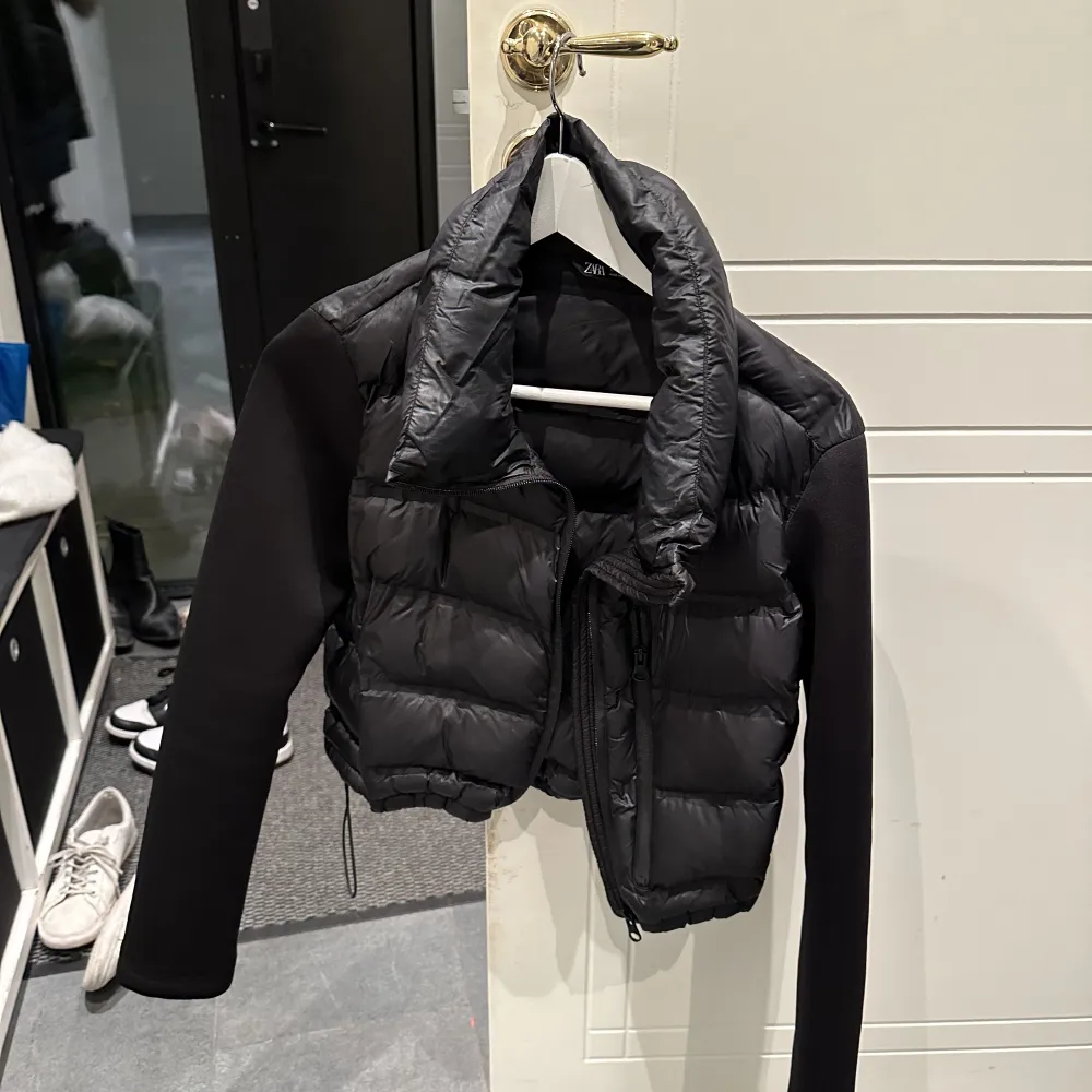 Quiltad jacka med hög krage. Långa ärmar i kombinerat neoprentyg. Framfickor. . Takit.