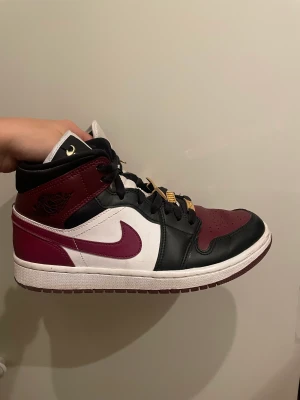 Jordan 1’s mid Dark beetroot gold pendant - Sälljer mina jordan 1’s mid i färgen dark beetroot, med guldsmycken på. Fint skick, men en pendant har lossnat från ena skon, men det är inget man tänker på och går säkert att fixa ny.  Storlek EU40  Köpta för 2999kr