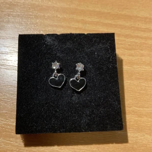 Örhängen  - Örhängen med små svarta hjärtan. De är aldrig använda med fina. Köpta i Korea :) Helt allergifria!