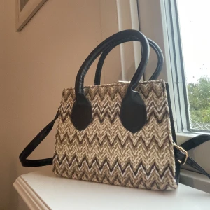 Väska  - liten, dålig kvalite. Väskan är av plast. Handtagen är lite snea 