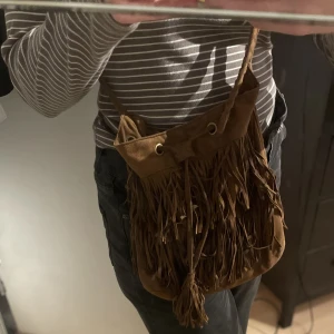 Mocka väska  - Fransad brun mockaväska från hm. Man kan justera axelbandets längd och spänna in (stänga) väskan- se sista bilden 