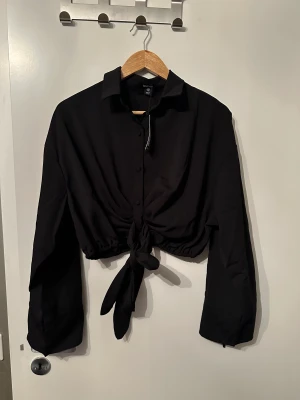 Kort skjorta med resår nertill  - En skjorta som är i mag tröja längd, man knyter den i mitten och den har även snören på årmarnarna som man kan knyta till, nytt skick, med prislapp kvar. 