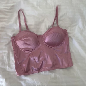 Korsett top - Rosa glansig Korsett / topp med dragkedja i bak. Lite noppig men tas bort om så önskas! Passar mig perfekt i kupan och omfång som vanligtvis har XS / 75B.✨Storlek M men upplevs mindre. 