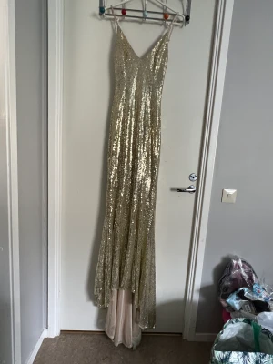 Klänning i Guld - Jättefin klänning i guld. Endast haft på mig den en gång till balen. Figursydd med en liten tail och öppen rygg. Kan justera band. Kan be om fler bilder! Passar mig perfekt , jag är 160 cm lång och brukar ha XS på kläder