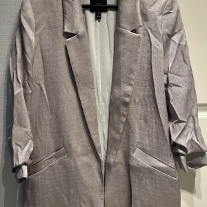 Kavaj - Kavaj i skimrande silver. Sparsamt använd. Tillhörande bälte medföljer som är i samma färg. Bälte ca 3 cm brett