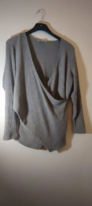 Grå tröja - Smickrande gråmelerad omlottröja i fint skick. Använd ett fåtal ggr.  Hund finns i hemmet.