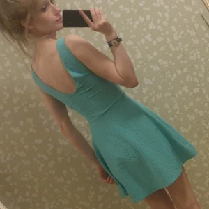 Turkos miniklänning med strukturvävt tyg och öppen rygg. - Miniklänning med struktur från H&M. Lågt skuren rygg och utställd kjol. Använd ett fåtal gånger och i mycket gott skick.