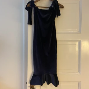 Velourklänning - Mörkblå velourklänning som sitter väldigt fint. Använd till ett antal middagar och fester! Den är knälång med band som man knyter som rosetter över axlarna. Bild från zalando