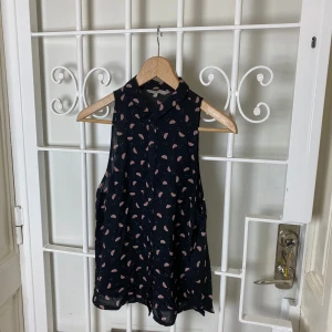 Svart blus med melonmönster – oanvänd - Mycket fint skick – oanvänd. Ärmlös.  Storlek: 42.  Bröstvidd: 96 cm. Längd: 64 cm. Bottenvidd: 118 cm. Axel till axel: 23 cm.  100 % viskos.