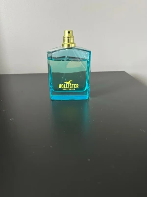 Blå parfym från Hollister - Fräsch parfym från Hollister i en fyrkantig, transparent blå glasflaska med guldfärgad spraykork. Flaskan har tydlig Hollister-logga i gult framtill och ger en somrig och ungdomlig känsla.