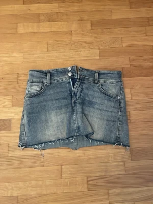 Jeanskjolskjorts från Bershka, blå denim - Säljer en jeanskjol från Bershka i storlek 36. De har råa, fransiga kanter, fem fickor och dubbla knappar i midjan. Klassisk denimlook med slitningar och normal passform. Det är en kjol men inbyggda skjorts. Den är nästan helt oanvänd och är i så bra skick😻