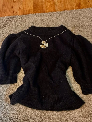 Svart stickad tröja Gina Tricot - Mysig svart stickad tröja från Gina Tricot med puffärmar och bred ribbad kant vid ärmslut och nederkant. Tröjan har en klassisk rund halsringning och är perfekt för dig som gillar en enkel men trendig look. Säljer inte halsbandet.