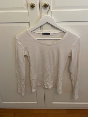 Vit långärmad topp från Zara - En enkel och stilren vit långärmad topp från Zara. Toppen har rund halsringning och är tillverkad i mjukt bomullsmaterial. Perfekt basplagg att matcha med olika outfits.