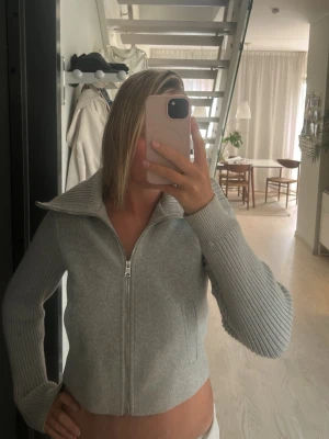 Ljusgrå zipjacka från Stradivarius - Trendig ljusgrå ziptröja från Stradivarius med bred krage och ribbade ärmar. Tröjan har dragkedja framtill och är tillverkad i mjukt material som känns skönt mot huden. Perfekt för lager på lager och en clean look.