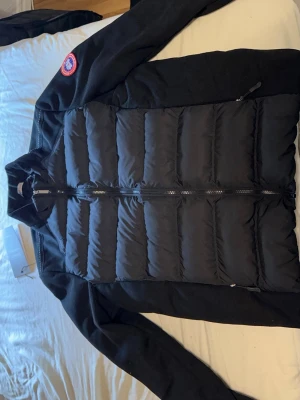 Svart hybridjacka från Canada Goose - Snygg svart cardigan från Canada Goose med quiltad framsida och dragkedja. Västen har en klassisk ståkrage och den ikoniska Canada Goose-loggan på axeln. Perfekt för hösten och håller dig varm under kyliga dagar. Tyvärr finns inte kvittot, därav det billiga priset. Däremot är den helt oanvänd och det är bara att höra av sig vid några funderingar.👉📩✅🤗Det står att jackan är i storlek L, men jag skulle säga att den sitter mycket mer som en M, speciellt om man har kläder under den..