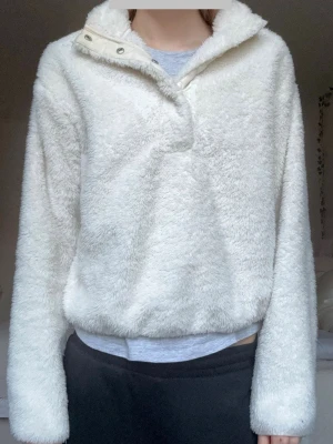Mysig Vit fluffig fleece-tröja med krage - Supermjuk och fluffig vit fleece-tröja med hög krage och knappdetalj vid halsen🩷Tröjan har långa ärmar och avslappnad passform, perfekt för kalla dagar! Enkel och stilren design som är lätt att matcha med andra plagg✨Jättegosig tjocktröja som passar bra som både mysplagg och vardagligt plagg🙏Använd flera gånger men i bra skick. Teddyfodret/fleece är fortfarande fluffigt! Hör av vid funderingar eller bud❤️