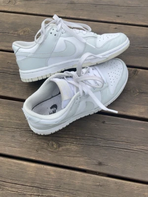 Nike Dunk Low sneakers - Säljer ett par Nike dunk Low sneakers. Storlek: 36.5, skorna är i bra skick, det enda som är skavt i Nike märket i sulan. Färgen är vit och ljusgrå