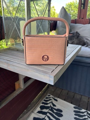 Beige/Rosa handväska  -  Superfin rosa/beige väska som passar till det mesta. Kommer ifrån Skoman men köpte på Smögen. Väskan har ett kortare band som är perfekt om man vill hålla väskan i handen men även ett längre axelband, som går att ta bort om man inte gillar det. För fler bilder eller diskussion om pris så bara skriv💗