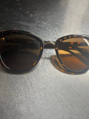 Bruna kattiga solglasögon!  - Snygga solglasögon med brunmelerad båge i klassisk cat eye-form. Glasen är mörka och bågarna har ett trendigt sköldpaddsmönster. Perfekta för soliga dagar och ger en cool vibe till din outfit.