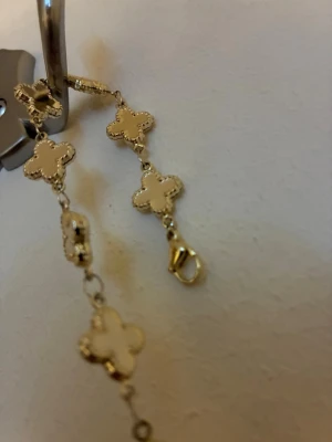 Guldfärgat armband med klöverhängen - Snyggt armband i guldfärg med flera fyrklöverformade hängen. Hängena har en pärlliknande kant och armbandet har en smidig karbinhake. Perfekt accessoar för dig som gillar detaljer och elegant design.