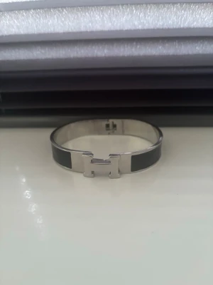 Silverfärgat armband med svart detalj - Snyggt armband i silverfärg med svart emalj och ett H-format spänne framtill. Armbandet har en stilren och modern design som passar till många olika looks. Materialet ser ut att vara metall med emaljerade partier.