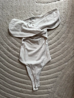 Vit off shoulder body från Zara - Trendig vit body från Zara med off shoulder-design och draperad överdel. Tillverkad i mjukt stretchigt material som sitter snyggt på kroppen. Perfekt för dig som vill ha en stilren och modern look.