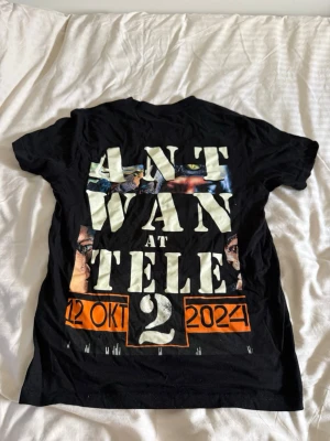 Svart Ant Wan T-shirt Tele2 Arena - Säljer en svart T-shirt med stort tryck på framsidan och text på baksidan från Ant Wan-konserten på Tele2 Arena 12 oktober 2024. T-shirten har korta ärmar och är i mjuk bomull. Perfekt för dig som gillar unika konsertplagg och streetwear.