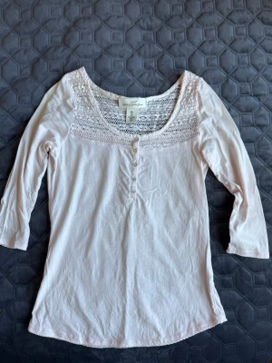 Ljusrosa blus med spets från H&M - Söt ljusrosa blus från H&M L.O.G.G. med spetsdetaljer upptill och knappar framtill. Blusen har trekvartsärm och rund halsringning. Liten foundationfläck på kragen som syns på sista bilden. För övrigt några sömmar som är trådiga men inget som syns så mycket 