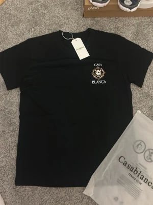 Svart t-shirt från Casablanca - Snygg svart t-shirt från Casablanca med tryckt logga och emblem på bröstet. Tröjan är i utmärkt skick och sitter som en smäck. Fraktar alltid inom 0-1 dagar!