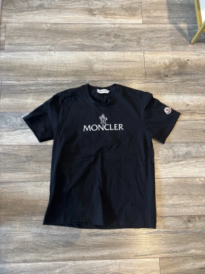 Svart Moncler t-shirt med logga - Snygg svart t-shirt från Moncler med stor vit logga på bröstet och klassisk rund hals. Kortärmad modell med Moncler-märke på ärmen. Perfekt för dig som gillar stilrena och exklusiva plagg.
