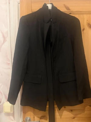 Svart kavaj med sjalkrage - Stilren svart kavaj med sjalkrage och långa ärmar. Kavajen har två fickor med lock framtill och en smal passform. Perfekt för dig som vill ha en klassisk och tidlös look.