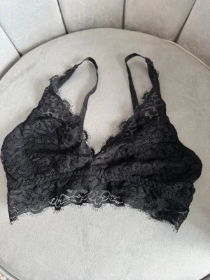 Svart spetsbralette med smala band - Säljer en svart bralette i mjuk spets med tunna axelband och vacker blommig spetsdetalj. Braletten har en feminin design utan bygel och är perfekt för dig som gillar en bekväm och stilren look. Materialet är genombruten spets som ger en romantisk känsla.