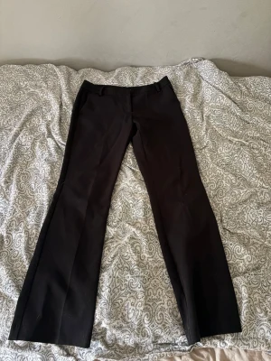 Svarta utsvängda kostymbyxor - Snygga svarta kostymbyxor med utsvängda ben och klassisk passform. Byxorna har hällor för skärp och två fickor baktill. Perfekta för en stilren look och passar till många olika outfits.