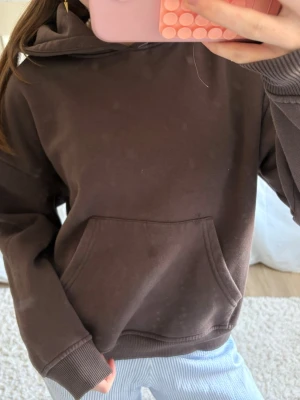Brun hoodie med magficka - Mysig brun hoodie med huva och stor magficka framtill. Tröjan har ribbade muddar vid ärmslut och nederkant. Perfekt för chill dagar och enkel att matcha med jeans eller mjukisbyxor.