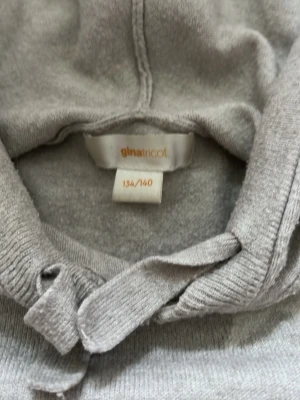 Grå hoodie med stjärna från Gina Tricot - Säljer en ljusgrå hoodie från Gina Tricot i storlek 134/140. Hoodien har en stor huva och en snygg stjärndesign på ryggen. Perfekt för dig som gillar enkel men cool stil.