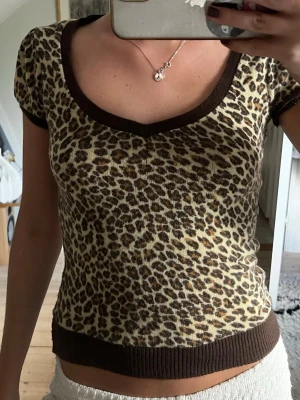 Leopardmönstrad topp - Säljer en leopardmönstrad topp med korta ärmar och v-ringning. Toppen har bruna ribbade kanter vid hals, ärmslut och nederkant. Är lite stickad i materialet och stretchig. Knappt använd, men köpt second hand! 