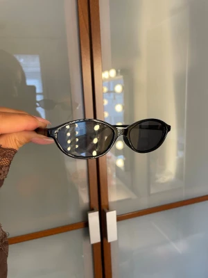 Svarta ovala solglasögon - Snygga svarta solglasögon med oval form och mörka glas. Bågarna är i plast och har en klassisk, stilren look som passar till många outfits. Perfekta för soliga dagar när du vill ha en cool vibe.