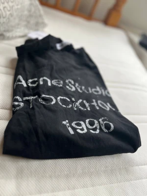 Long sleave Acne Studios 1996 - Long sleave från Acne Studios med vitt tryck framtill där det står 'Acne Studios STOCKHOLM 1996'. Klassisk modell med rund hals och kort ärm. Snygg och enkel design som funkar till det mesta. Inte tshirt long sleave