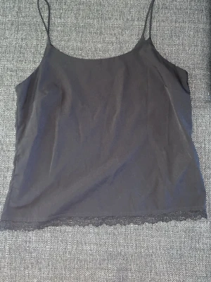 Svart linnetopp med spetskant - Säljer en svart linnetopp med tunna axelband och snygg spetskant längst ner. Toppen har en enkel och stilren design som passar perfekt till många olika outfits. Materialet känns mjukt och lätt mot huden.