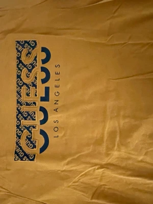 Gul GUESS t-shirt med blå logga - Snygg gul t-shirt från GUESS med stor blå logga och mönstrad detalj framtill. T-shirten har klassisk passform och rund halsringning. Perfekt för dig som vill sticka ut med en färgglad och trendig look.