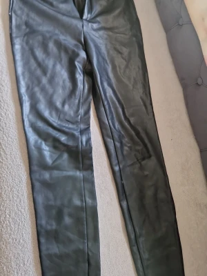 Svarta skinnbyxor från Sisters Point - Snygga svarta skinnbyxor från Sisters Point med klassisk femficksmodell och dragkedja fram. Byxorna har en rak passform och är perfekta för dig som vill ha en edgy look. Materialet är mjukt och följsamt för extra komfort.