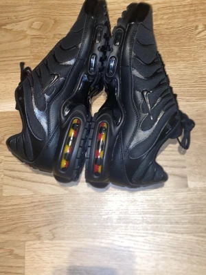 Svarta sneakers med luftbubbla - Snygga svarta sneakers med vågiga detaljer och synlig luftbubbla i sulan med gula och röda inslag.  Helt nya.. Skorna har en sportig look med mesh och syntetmaterial, samt robust yttersula för bra grepp. Perfekta för dig som gillar streetwear och vill sticka ut.